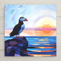 Geometric low-poly style ceramic art tile of a puffin on a rock at ocean sunset in angular blue orange and purple facets, modern scandinavian coastal seabird wall decor.