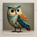 A whimsical folk-style owl ceramic tile featuring a wide-eyed owl decorated with layered autumn leaves and textured patterns in teal, orange, and cream tones. The square tile has a storybook illustration style with a calm, charming expression, making it ideal as nature-inspired wall decor or a gift for owl lovers.