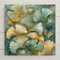 A botanical ginkgo wall art ceramic tile featuring layered fan-shaped ginkgo leaves in soft teal, pale green, and warm gold tones. The stained glass style design has fine linework and a calm, airy composition. This is a permanent print on ceramic tile, not real stained glass. Optional wall hanger, easel stand, cork backing, and premium frame options are available.