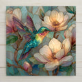 Stained glass style ceramic tile featuring a vibrant emerald and turquoise hummingbird hovering among soft ivory and blush magnolia flowers. Pastel teal background with delicate gold leading creates romantic cottagecore botanical wall art for bird lovers and garden home decor.