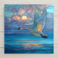 Stained glass style swan in flight ceramic tile with wings fully extended over deep cobalt and teal water at golden hour, warm gold and amber light catching the spread feathers, a vivid wildlife bird and nature lover gift.