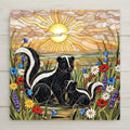 Stained glass style ceramic tile featuring a mother skunk and baby skunk surrounded by red poppies, daisies, lavender, and bluebells under a glowing golden sunrise. Woodland wildlife wall art ceramic tile designed for rustic cottage decor and nature home decor.