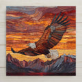 A stained glass–style ceramic tile featuring a soaring bald eagle above glowing sunset mountains in vivid amber, red, and gold tones.