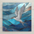 White tern with black cap and red beak in flight over layered turquoise and deep blue ocean waves in stained glass style, coastal ceramic tile wall art.