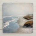 A calm coastal wall art ceramic tile featuring a foggy beach shoreline with gentle waves and soft dune grasses. This serene ocean-inspired home decor piece creates a peaceful, minimalist coastal feel. The artwork is a permanent print on ceramic tile, not real stained glass. Optional tile wall hanger, easel tile stand, cork backing, and premium frame options are available.