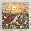 Stained glass style ceramic art tile of a mother hedgehog and baby hedgehog in a wildflower meadow of poppies daisies and lavender at sunrise, woodland nursery and baby shower decor.