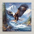 Audubon-style ceramic tile of a bald eagle with a fish wall art in flight over a mountain river. A bold wildlife home decor scene perfect for lodge, cabin, or patriotic décor.