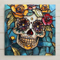 Stained glass style ceramic art tile of a Day of the Dead sugar skull with yellow and red roses and dark floral eyes on a teal-green leaded-glass background — a Dia de los Muertos decoration.