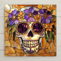 Stained glass style ceramic art tile of a Day of the Dead sugar skull with purple flowers and purple eye-sockets on a warm amber and gold leaded-glass background — a Dia de los Muertos decoration.