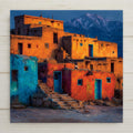 Stained glass style Taos New Mexico ceramic tile depicting the historic Taos Pueblo adobe structures rising in terraced earthen tiers against the Sangre de Cristo Mountains and a deep cobalt sky, rendered in jewel-tone ochres, terracotta, and cobalt blues.