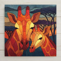 Ceramic art tile depicting a mother giraffe nuzzling her calf on the African savanna at sunset, rendered in jewel-tone stained glass style with warm golden tones and acacia silhouettes