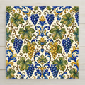 A flowing majolica grapevine with grape clusters, curling tendrils, and broad leaves in cobalt blue, golden yellow, and sage green on a soft cream tile.