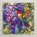 Stained glass style ceramic tile of a ruby throated hummingbird hovering at cascading purple wisteria blossoms with green leaves and golden light, luminous floral bird wall art