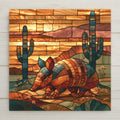 Stained glass style ceramic tile of an armadillo with banded shell walking past tall saguaro cacti under a golden desert sunset sky
