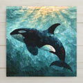 Sea glass style ceramic tile of an orca in profile gliding through soft aqua water with light rays from above in frosted black white and seafoam glass