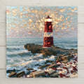 Sea glass style ceramic tile of a lighthouse built from red and white sea glass pebbles standing on rocks above real ocean waves beneath a cream glass mosaic sky