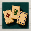 Three mahjong dragon tiles with a red character a green malachite character and a blank white dragon in a blue border on teal felt on a square ceramic art tile
