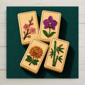 Four mahjong flower tiles plum blossom orchid chrysanthemum and bamboo inlaid in coloured stone and gold on teal felt on a square ceramic art tile