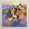 Ceramic art tile of two donkeys nuzzling forehead to forehead in a blooming purple lavender field, drawn with leaded glass style panes, with a Provence farmhouse and cypress trees on the golden hillside behind