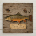 Brook trout ceramic tile art in vintage specimen plate style with a hand-painted-style brook trout, tied fly fishing flies and an aged paper name label on weathered barnwood