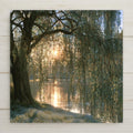 Ceramic art tile of a weeping willow beside calm water at soft dawn, morning light glowing through leaded glass style branches, with a carpet of blue forget me not flowers on the bank