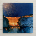 Hoover Dam ceramic art tile in an alcohol ink style — night scene with a cobalt and violet starry sky speckled in gold above the warmly lit dam and dark canyon water.