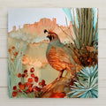 Alcohol ink style ceramic art tile of a Gambel's quail with its black teardrop plume perched on red rock, blue agave and a cactus trunk beside it, red desert blooms below and salmon-colored cliffs behind under a pale sky